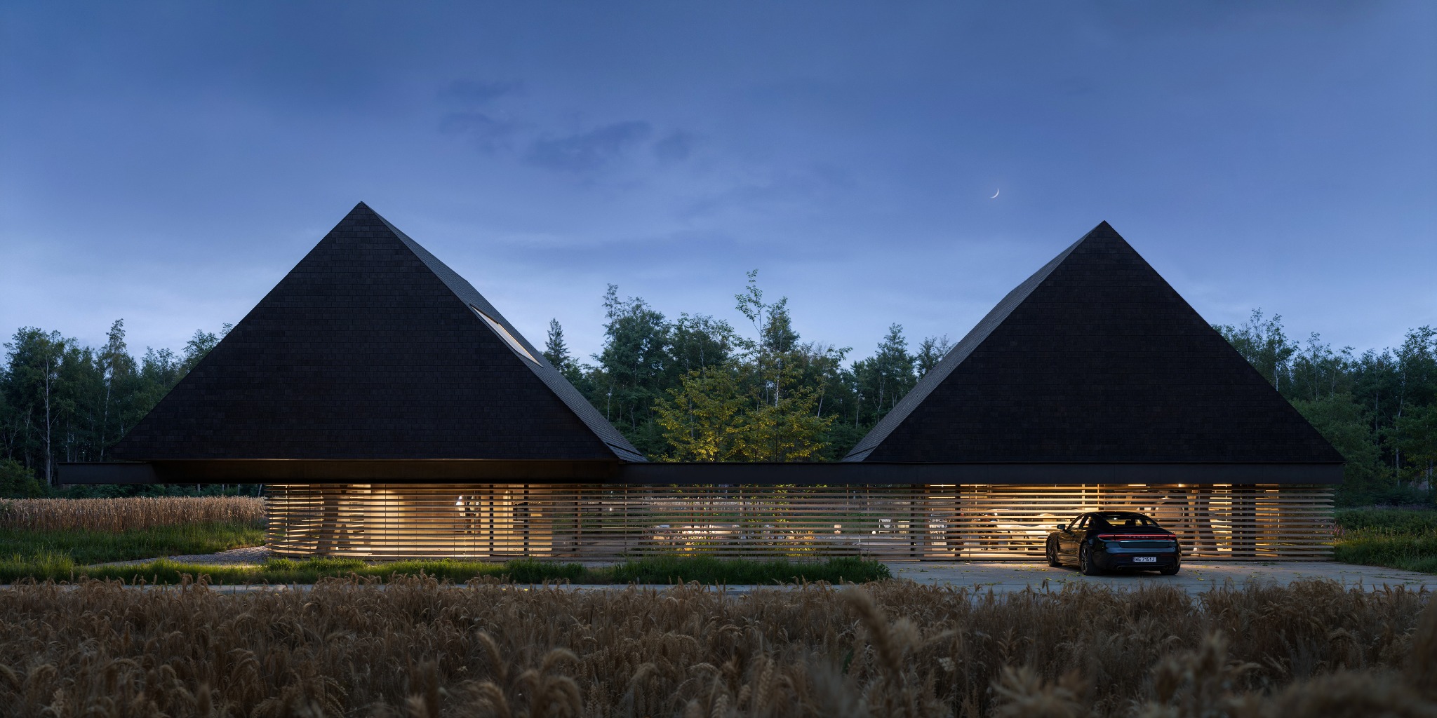 Nowoczesny dom z piramidalnym dachem oświetlony wieczornym światłem, z widocznym samochodem i polem zboża w tle. Unikalna architektura.