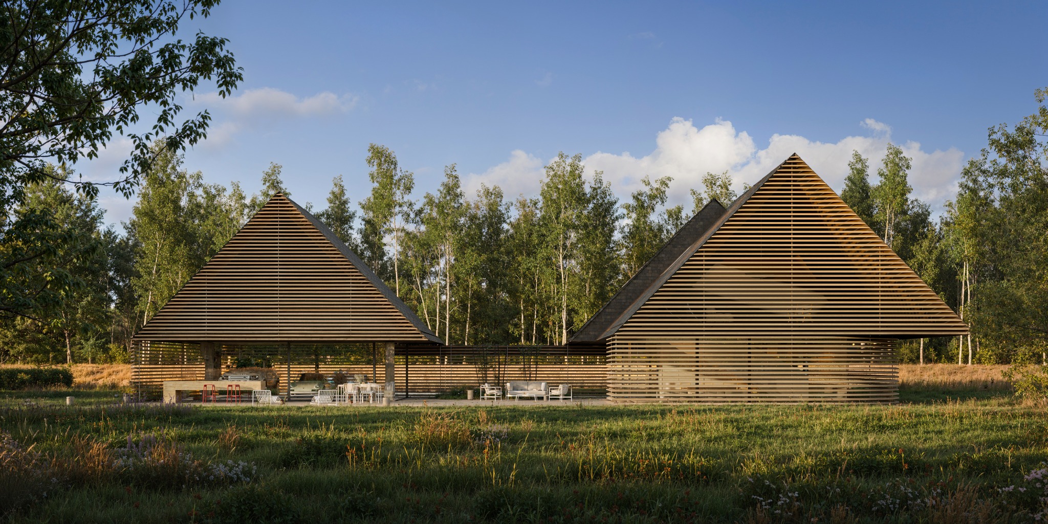 Awangardowy dom z drewnianą elewacją w kształcie piramidy, otoczony zielenią i drzewami. Widoczne meble ogrodowe i elementy wyposażenia wnętrz.