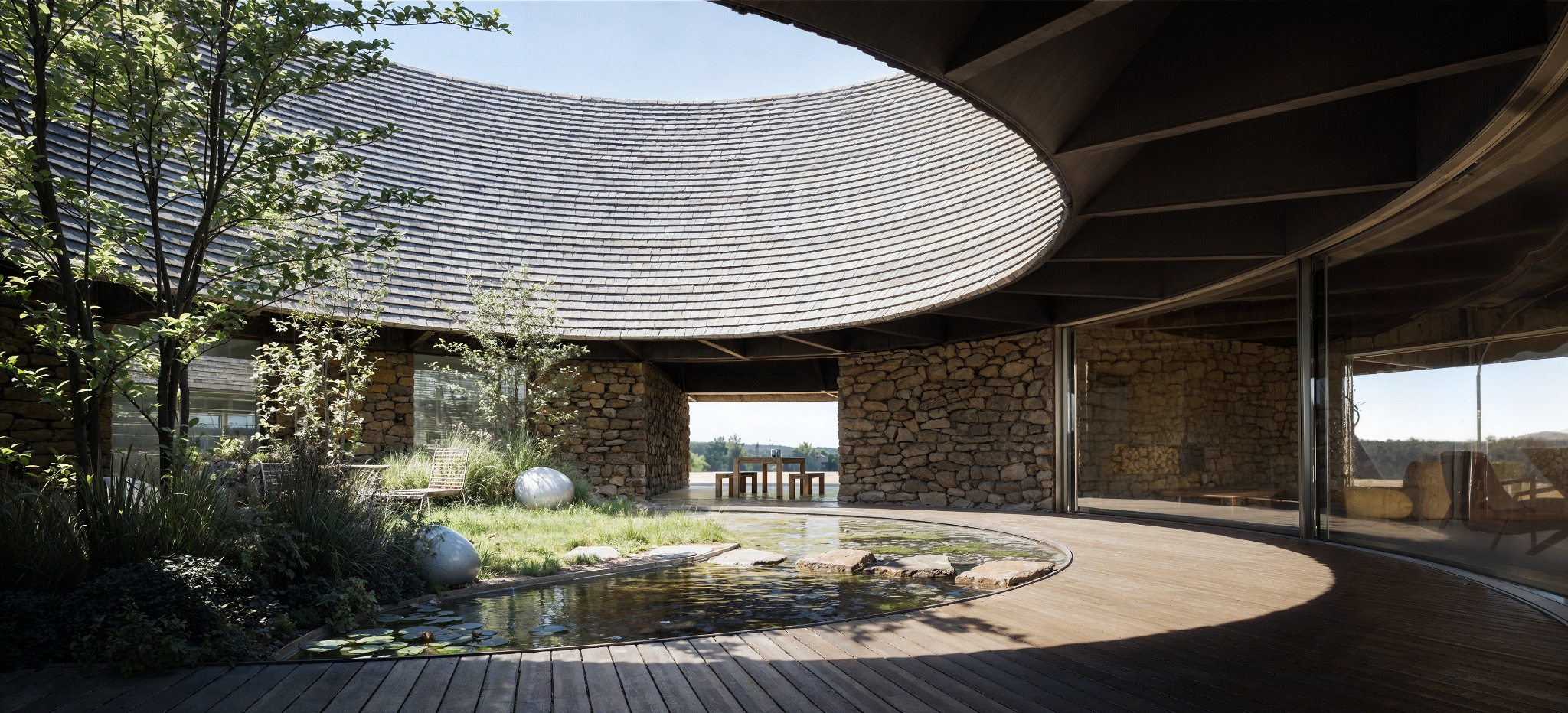 Unikalny dom z kamienia i drewna, z okrągłym dachem krytym gontem i wewnętrznym oczkiem wodnym. Nowoczesna architektura z naturalnymi materiałami.