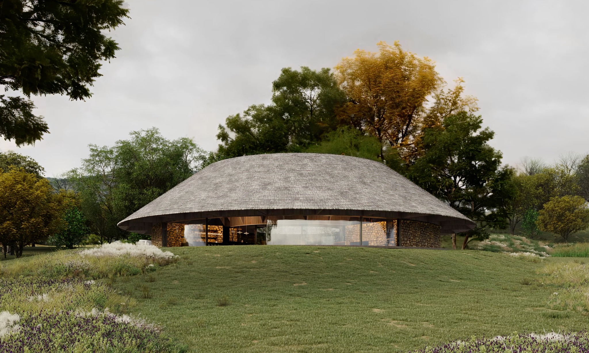 Nowoczesny, okrągły dom z kamienia i drewna, kryty gontem, wkomponowany w zielony krajobraz. Duże przeszklenia zapewniają naturalne światło. Architektura ekologiczna.