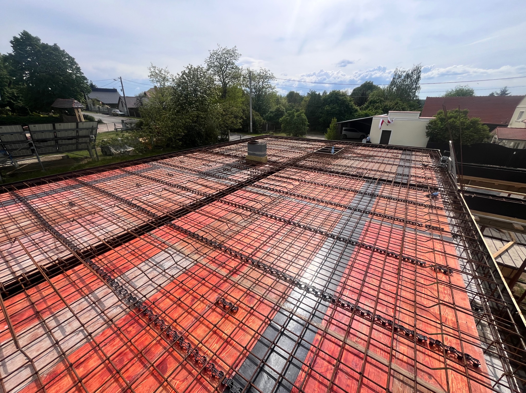 Zbrojenie stropu na deskowaniu, widok z góry na przygotowaną konstrukcję z siatki stalowej przed betonowaniem, z kominem wentylacyjnym w tle.