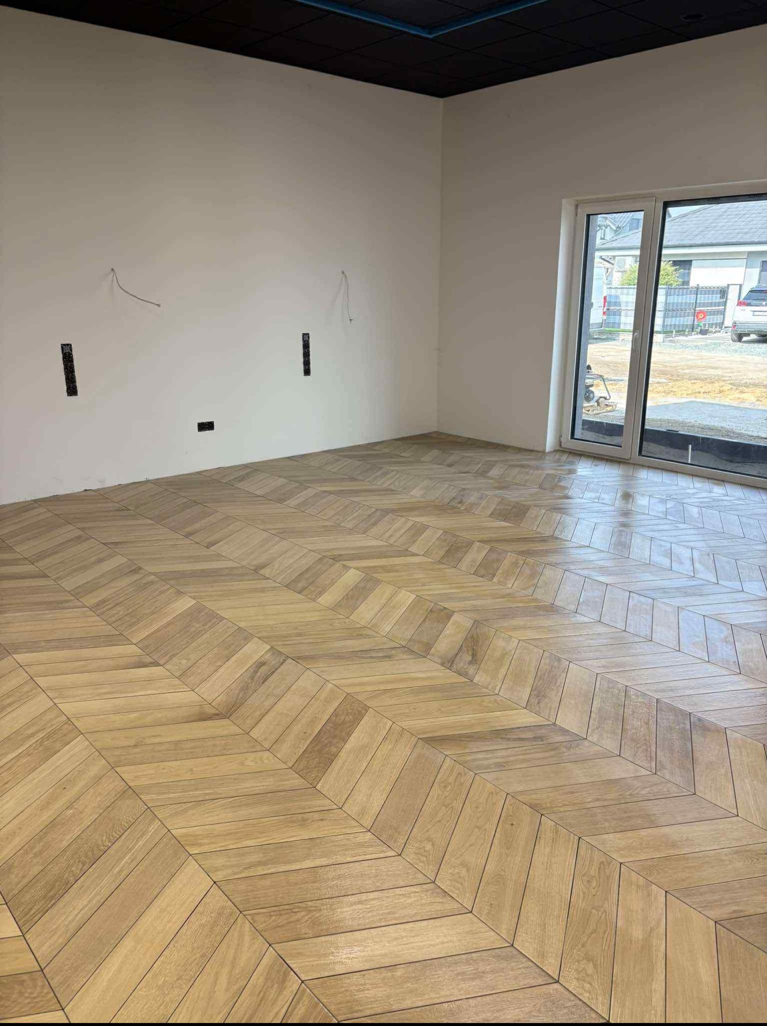 Ukończona podłoga z płytek imitujących drewno ułożonych we wzór jodełki w Lesznie. Widoczne gładkie, jasne ściany i duże okno.