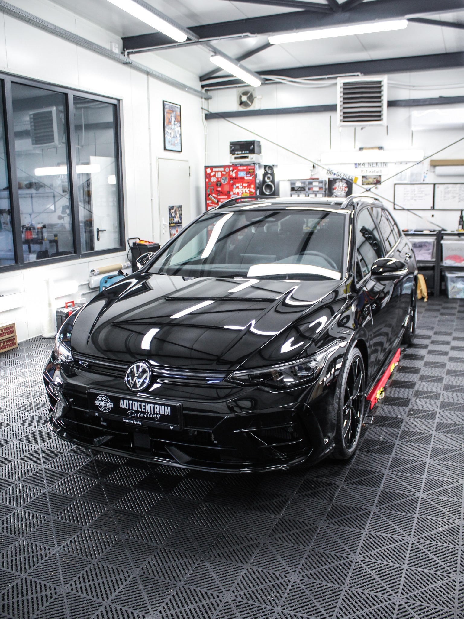 Błyszczący, czarny VW kombi po detailingu w studiu. Widoczne logo Autocentrum Detailing na tablicy rejestracyjnej, czarne felgi i czerwone akcenty na progach.