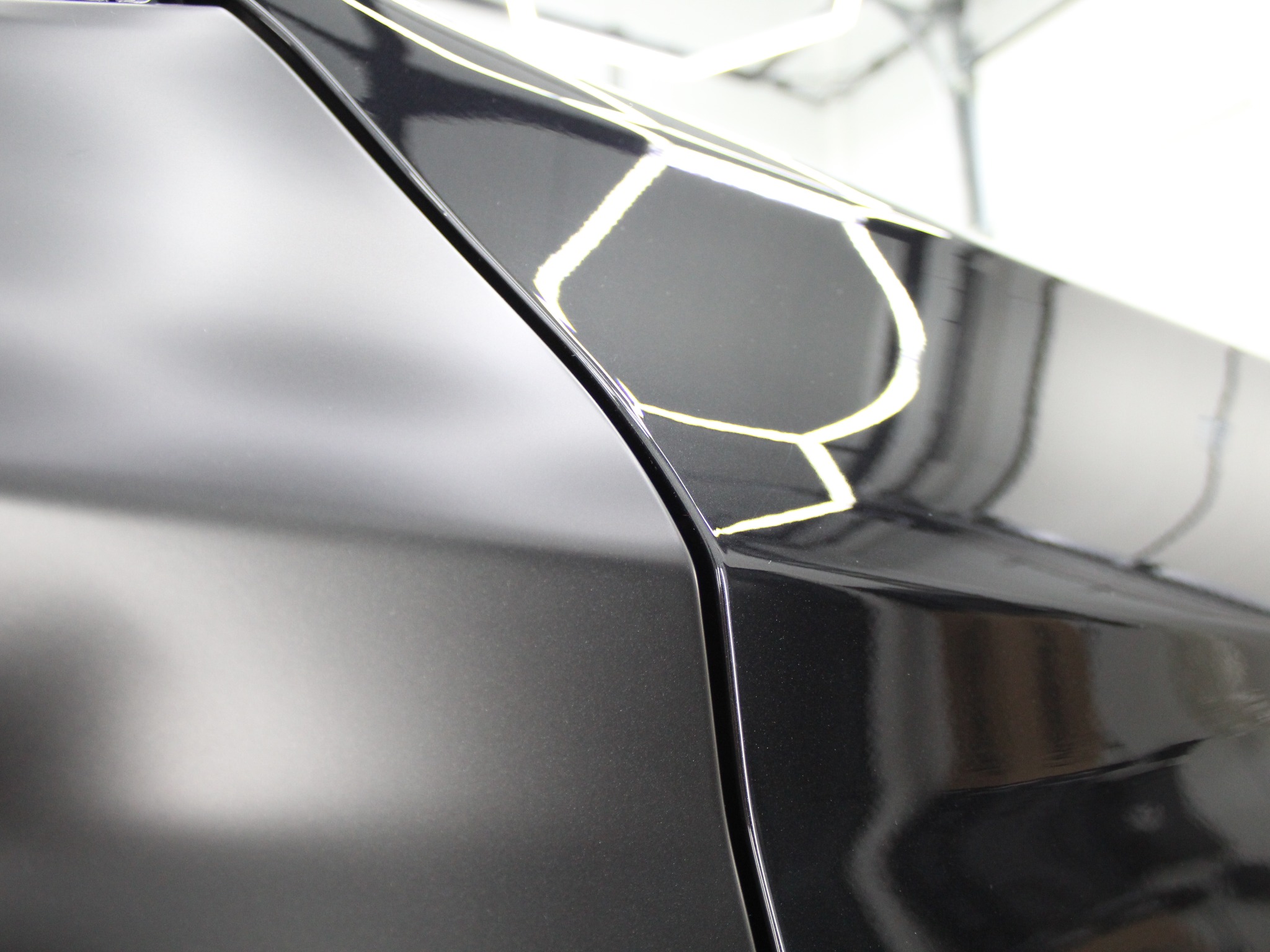 Błyszczący, grafitowy bok samochodu po detailingu, z wyraźnym odbiciem światła. Widoczna linia łączenia elementów karoserii. Gładka powierzchnia.