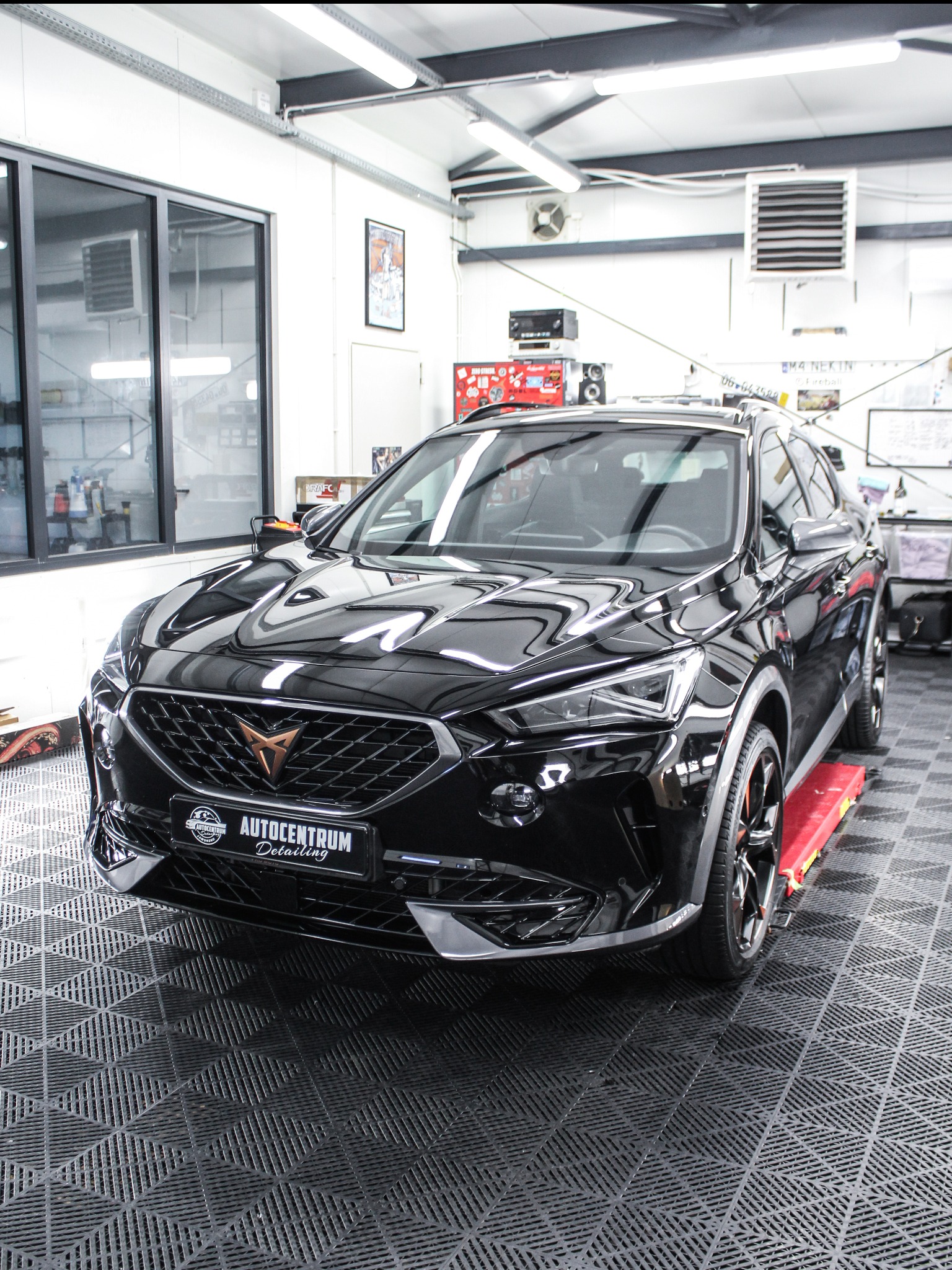 Błyszczący, czarny samochód Cupra na podnośniku w warsztacie detailingowym w Jaworznie. Widoczne logo Autocentrum Detailing na tablicy rejestracyjnej.