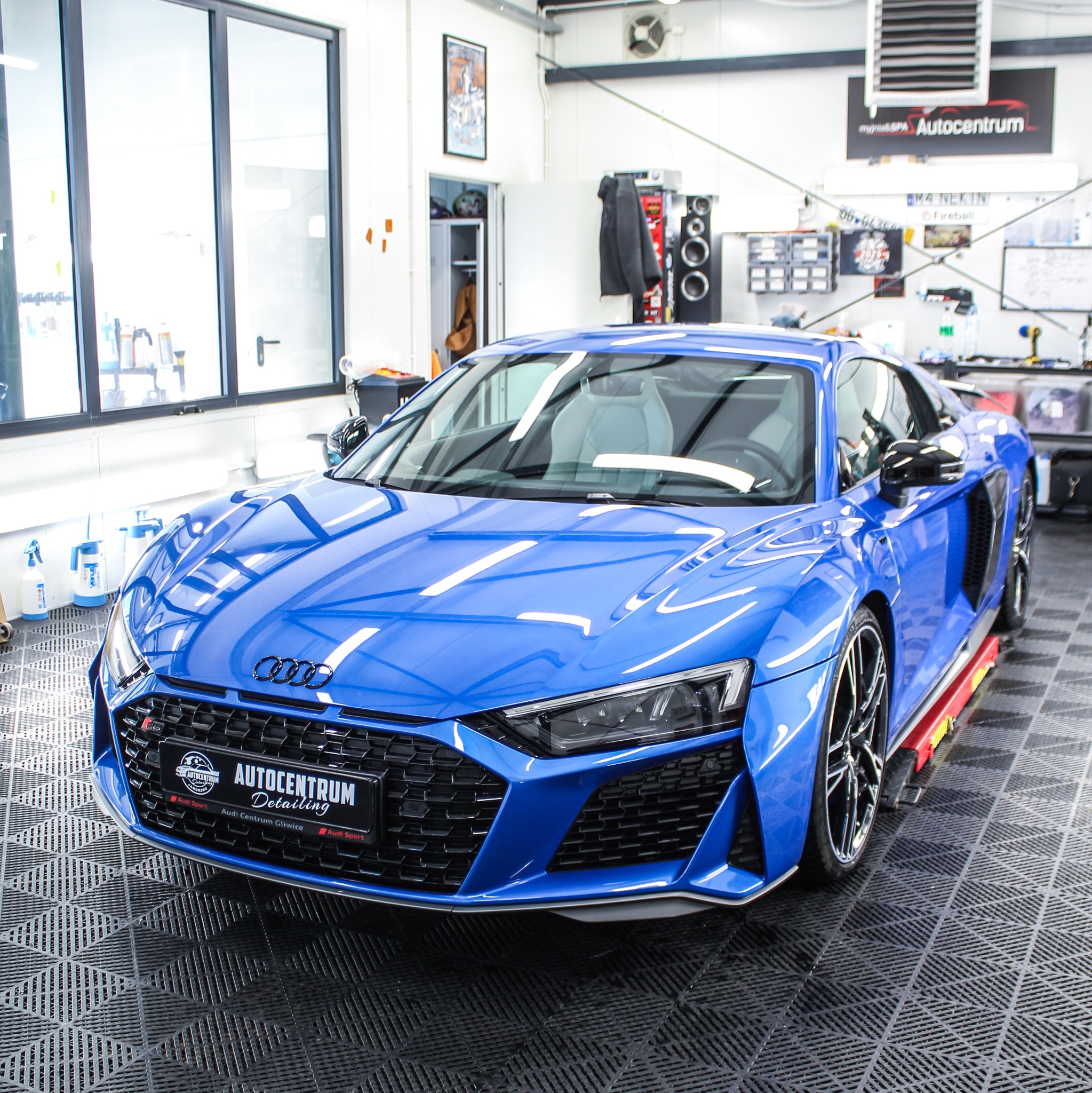 Błękitne Audi R8 po detailingu w studiu Autocentrum Gliwice, z widocznym logo firmy na grillu. Auto stoi na podnośniku w czystym, dobrze oświetlonym warsztacie.