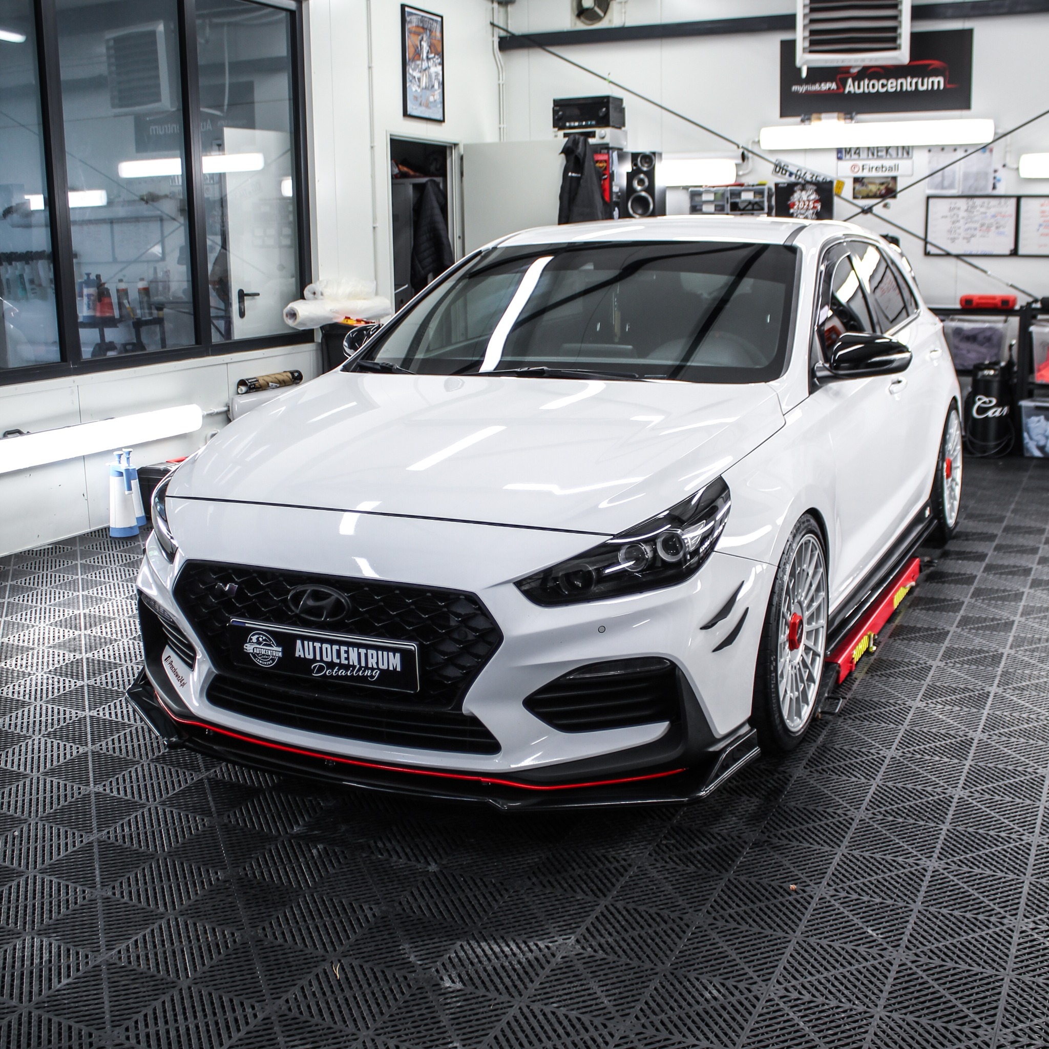 Biały Hyundai i30 N po detailingu, z czarnymi akcentami i czerwonym paskiem na dolnej krawędzi. Auto stoi w profesjonalnym studiu detailingu na podnośniku.