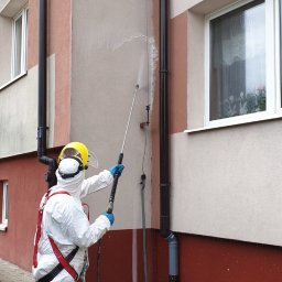 Rensar Polska - Pracownik w kombinezonie ochronnym czyści elewację budynku z użyciem myjki ciśnieniowej. Widoczne zacieki i piana po czyszczeniu.