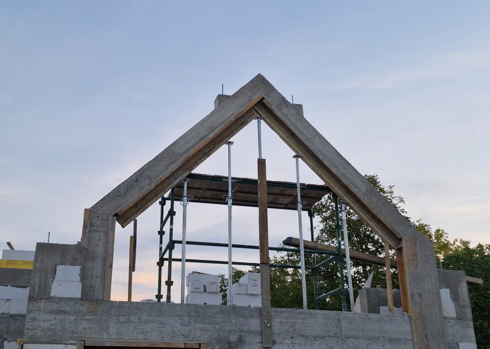 Wznoszenie betonowej konstrukcji domu jednorodzinnego. Widoczne szalunki i podpory stropu. Ściany z betonu komórkowego. Budowa w toku przy pogodnym niebie.