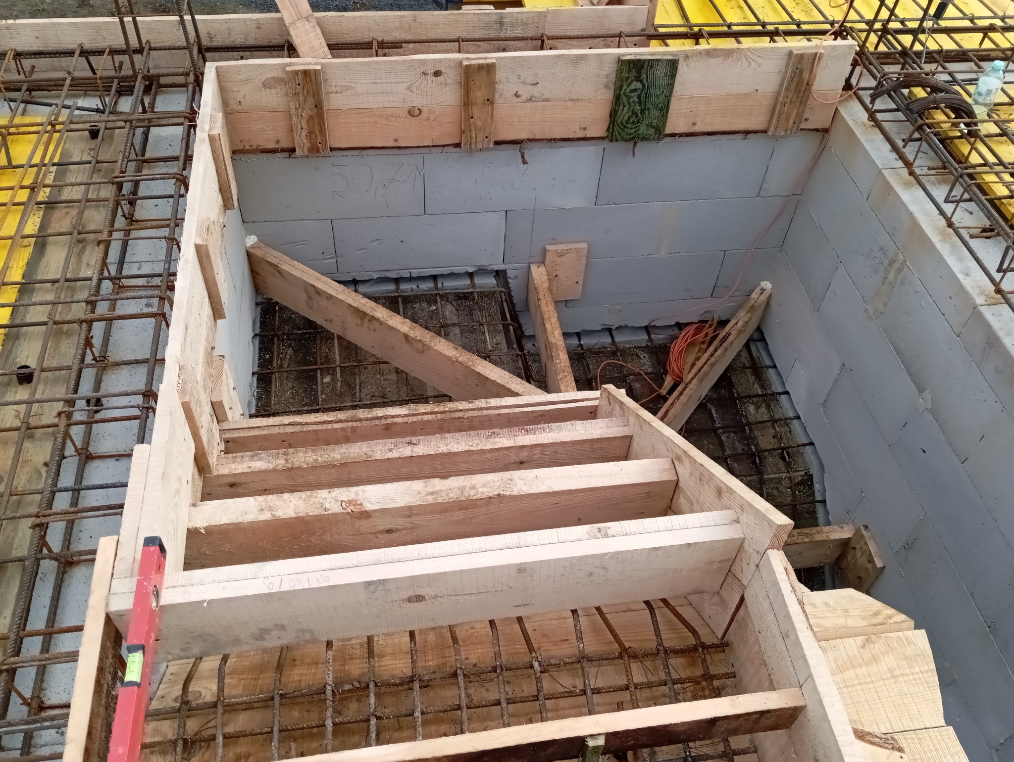 Szczegółowy widok z góry na szalunek schodów z drewnianych desek i zbrojenia, przygotowany do zalania betonem, z użyciem bloczków betonowych.