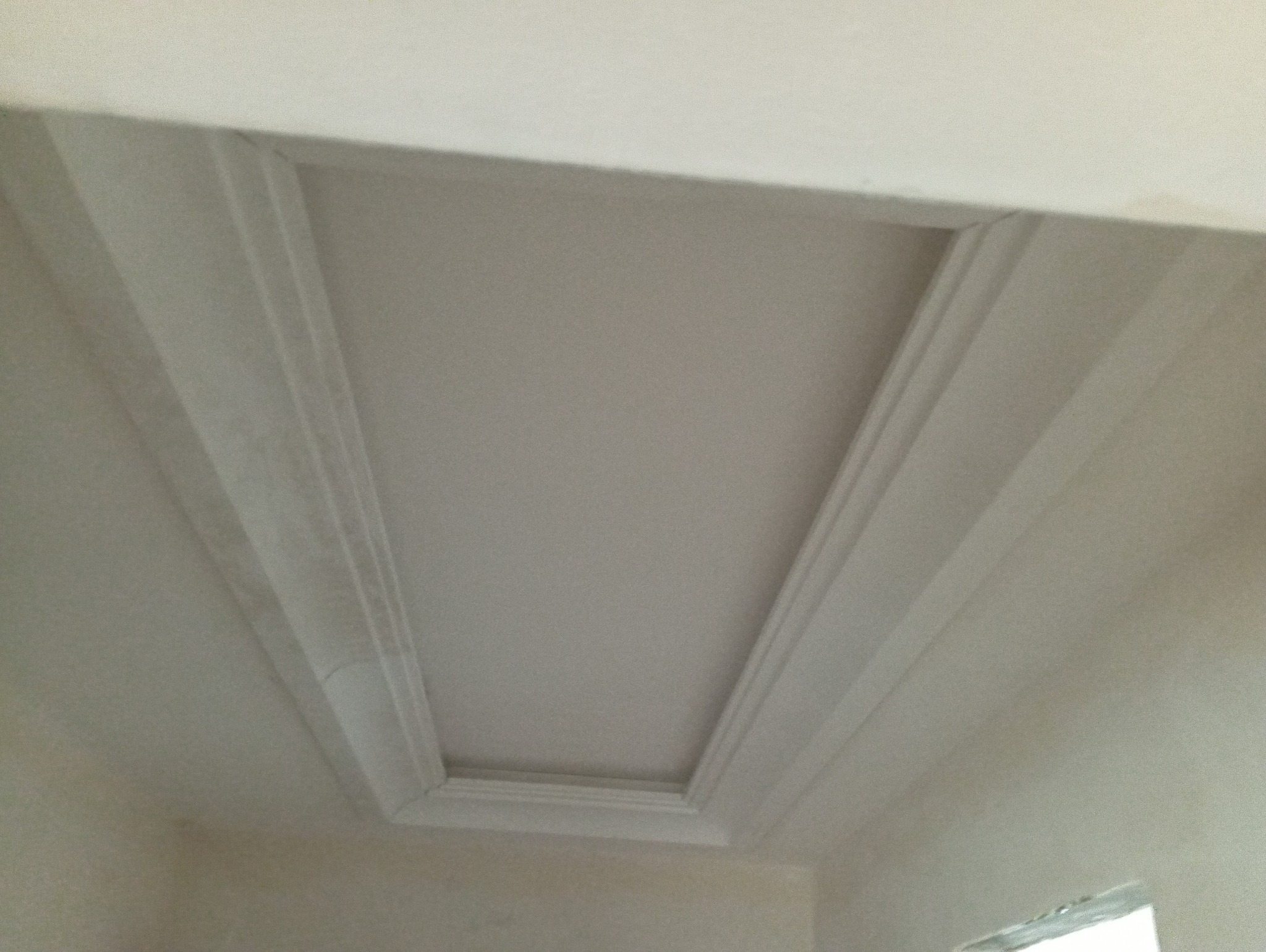 Wykończony sufit z dekoracyjnymi listwami w odcieniach bieli, tworzący geometryczny wzór. Ujęcie z dołu, podkreślające detale wykończenia i symetrię.
