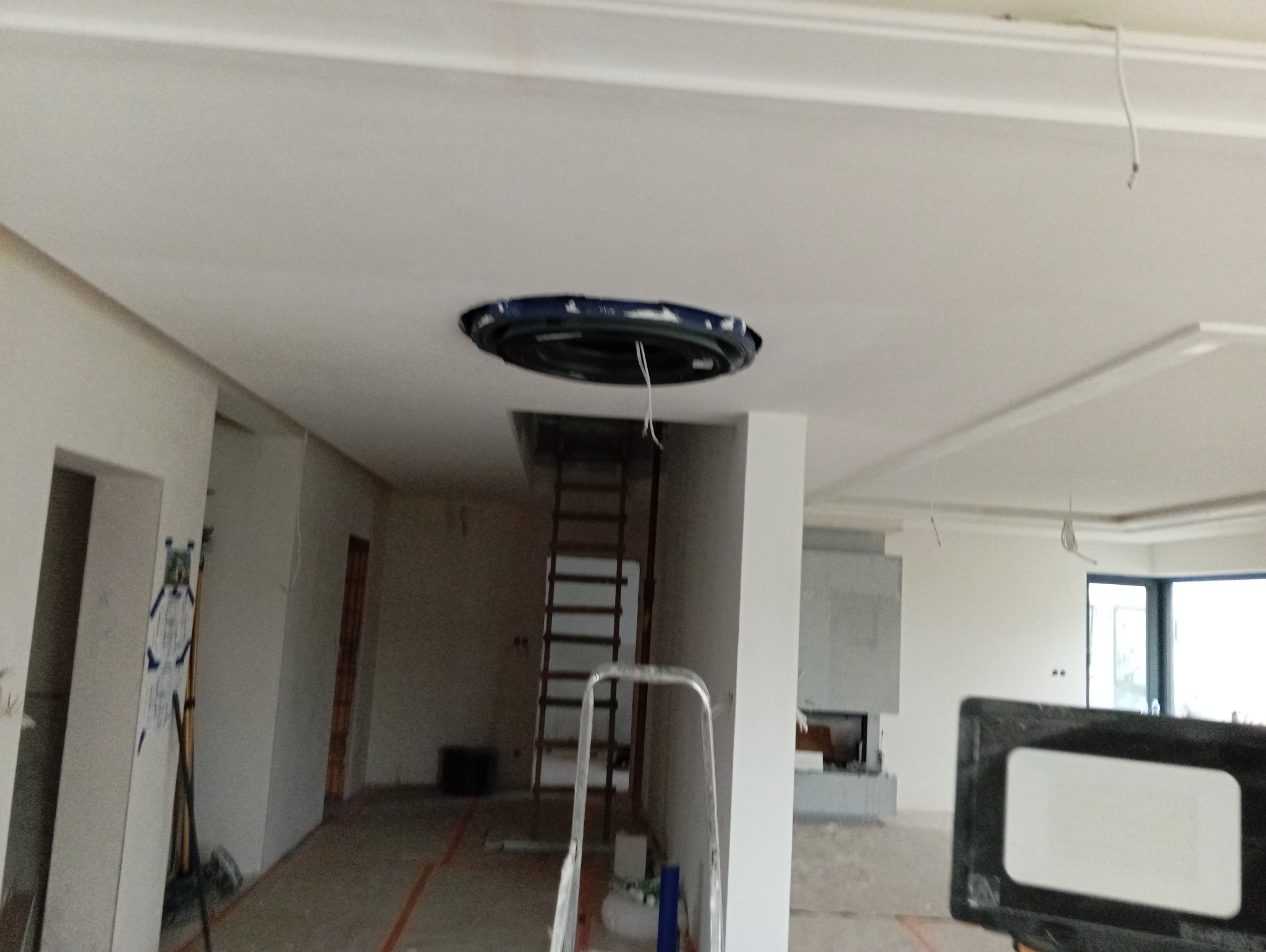 Wnętrze w trakcie remontu: biały sufit z otworem na oświetlenie, widoczne przewody, drabina w tle, ściany przygotowane do malowania. Prace wykończeniowe w nowym domu.