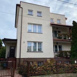 Sunclean - mycie elewacji, dachów, paneli fotowoltaicznych - Trzykondygnacyjny dom z beżową elewacją, balkonami z kutymi balustradami i numerem '21' na ścianie, widziany zza metalowego ogrodzenia.
