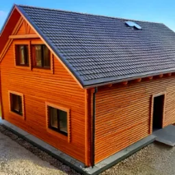 Drewniany dom z ciemnym dachem na tle zieleni i błękitnego nieba. Widok z góry ukazuje strukturę drewna i detale wykończenia. Nowoczesny design w naturalnym otoczeniu.