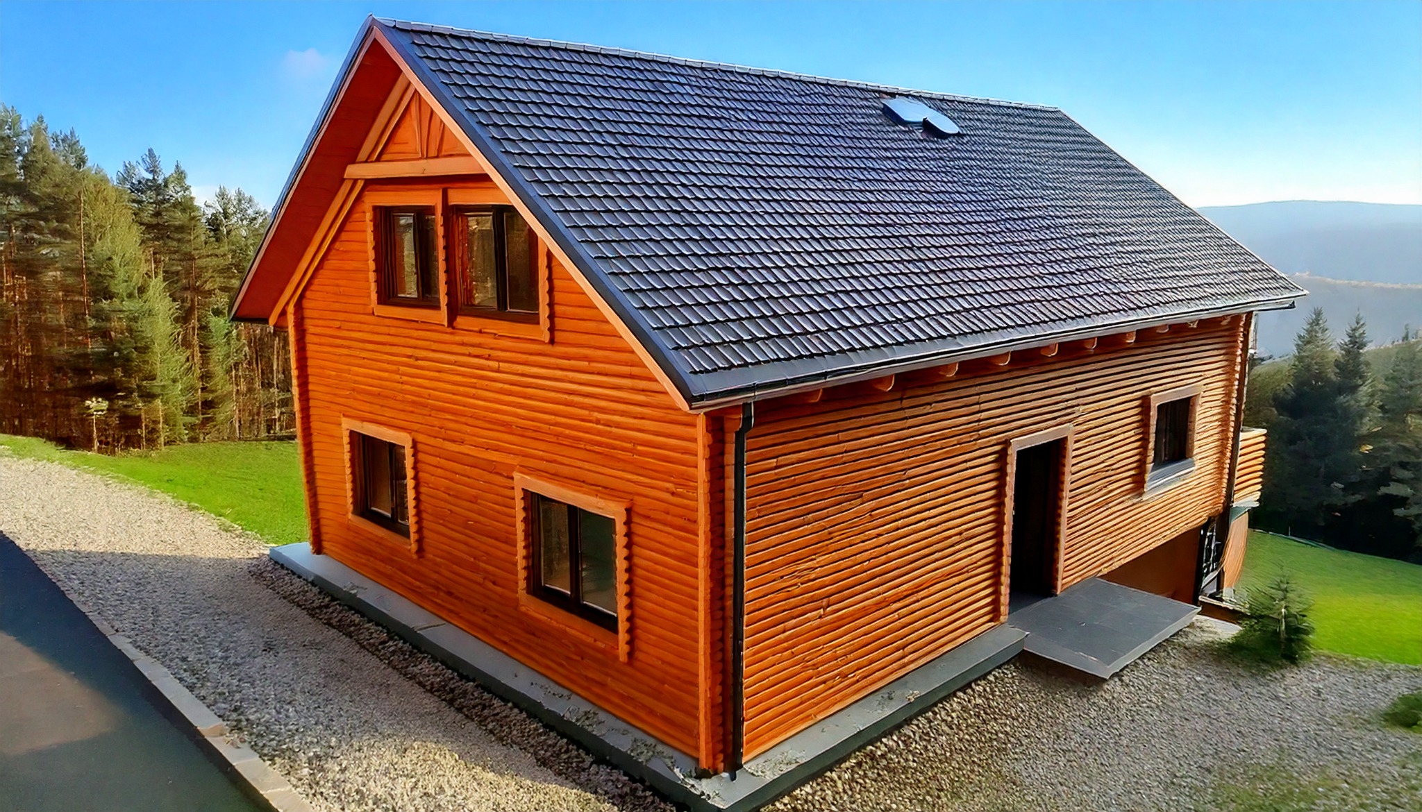 Drewniany dom z ciemnym dachem na tle zieleni i błękitnego nieba. Widok z góry ukazuje strukturę drewna i detale wykończenia. Nowoczesny design w naturalnym otoczeniu.