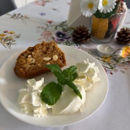 Bistro Frelka i Hanys - Kawałek ciasta orzechowego z bitą śmietaną i miętą na białym talerzu, dekoracja stołu z kwiatami i szyszkami w tle.