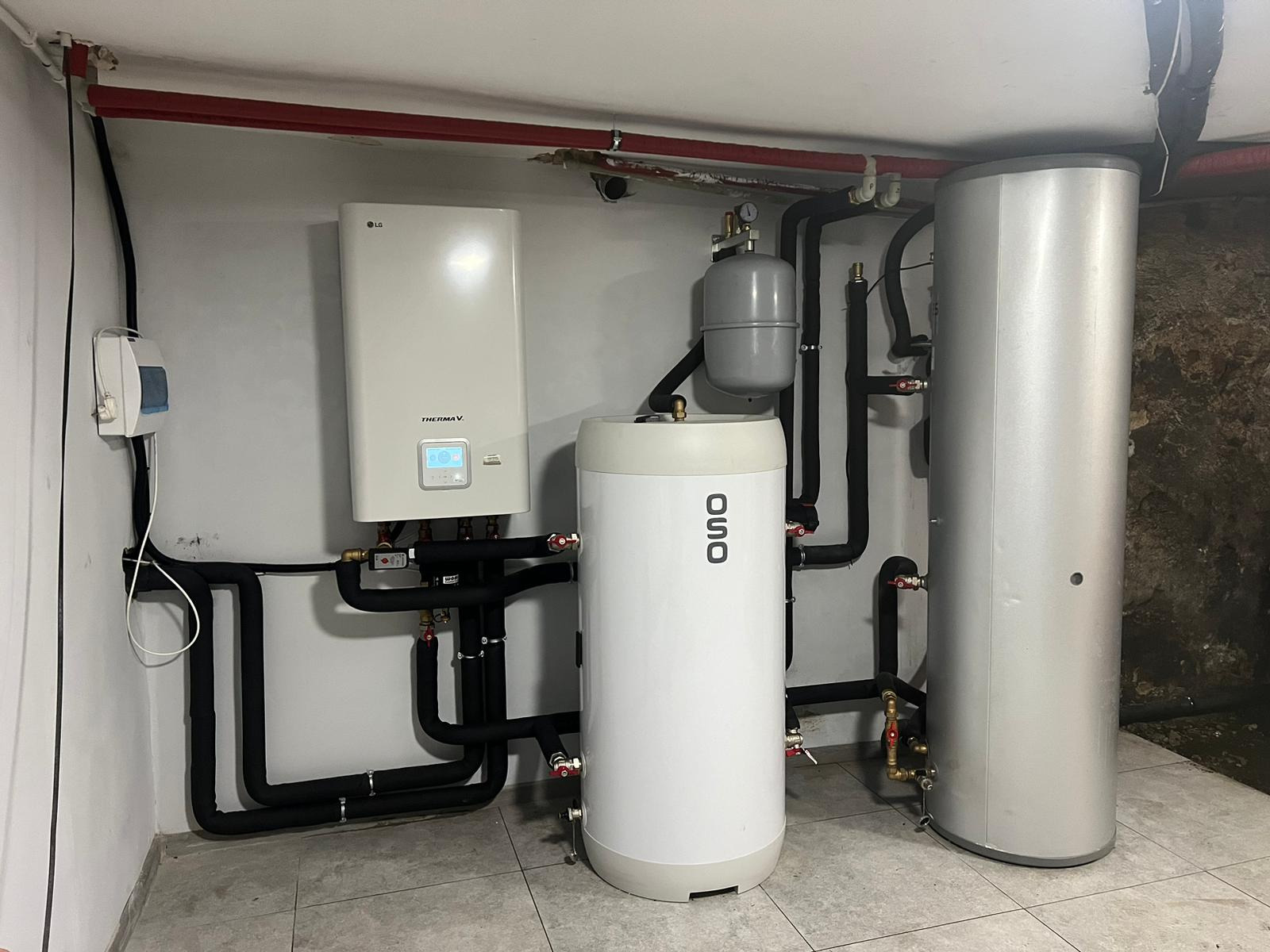 Zestaw grzewczy w kotłowni: biały zasobnik OSO, pompa ciepła LG Therma V z wyświetlaczem, czarne rury instalacyjne, szary zbiornik wyrównawczy.