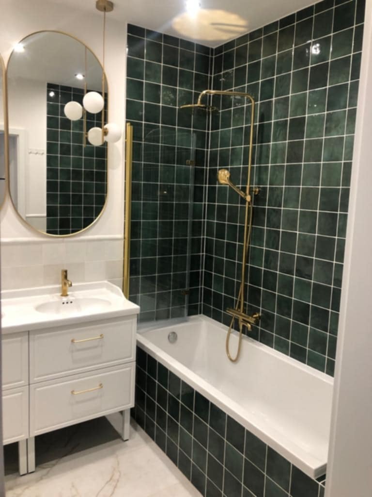 Nowoczesna łazienka z zielonymi płytkami, złotą armaturą i owalnym lustrem. Biała umywalka z szafką i marmurowa podłoga tworzą elegancki wystrój.