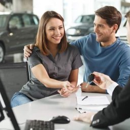 Anna Ciślak - Uśmiechnięta para odbiera kluczyki do nowego samochodu od sprzedawcy w salonie. W tle widoczne inne modele aut.