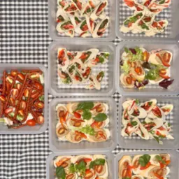 Różnorodne przekąski cateringowe w plastikowych pojemnikach na czarno-białym obrusie w kratę. Wrapy z warzywami, sałatka z kabanosami i grzanki z pastą.