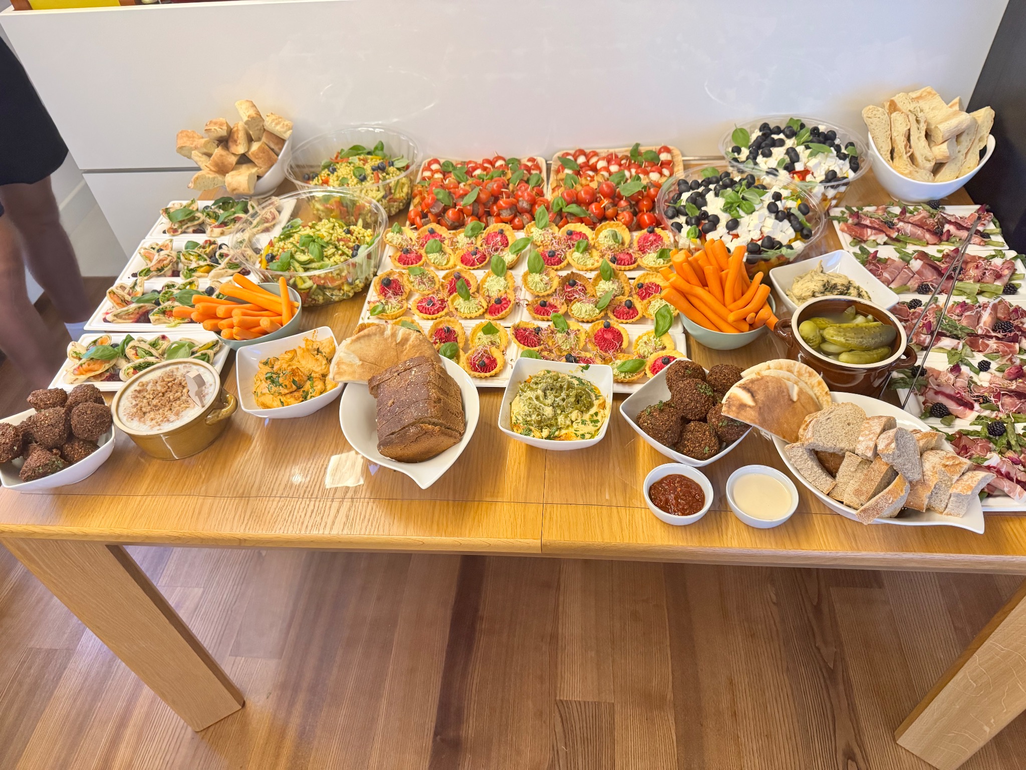 Stół bufetowy uginający się pod ciężarem różnorodnych przekąsek: tartaletek, sałatek, pieczywa i warzyw. Bogata paleta barw i tekstur, idealna na imprezę.