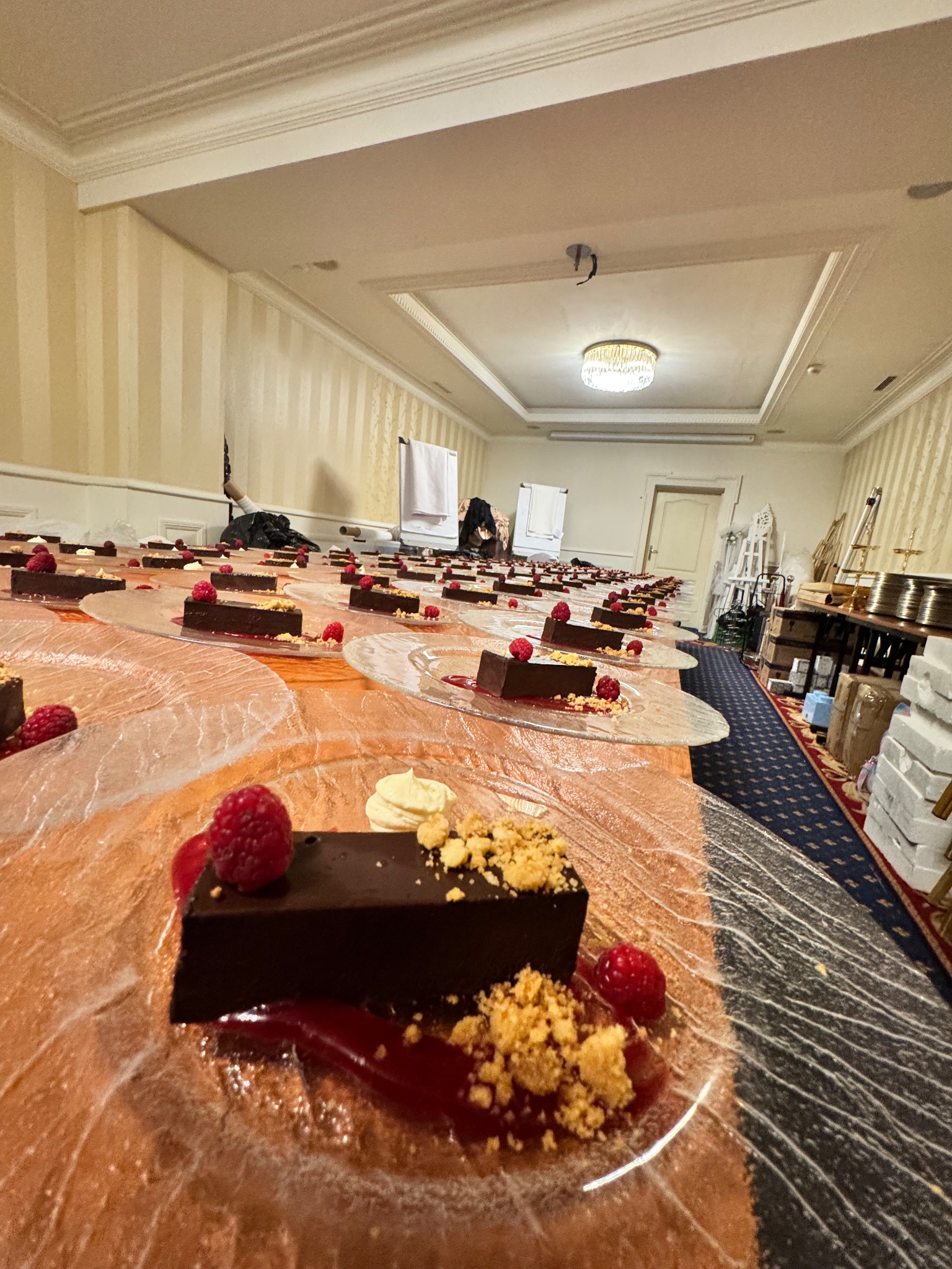 Długi stół z deserami: czekoladowe ciastka z malinami i kruszonką na szklanych talerzach. Eleganckie wnętrze, gotowe do serwowania. Perspektywa z bliska.