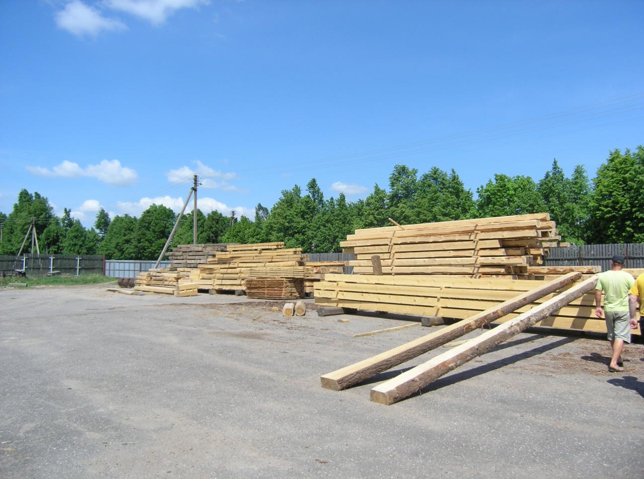 Składowane drewno budowlane: deski i belki z korą, przygotowane do budowy, widoczne na placu pod błękitnym niebem.
