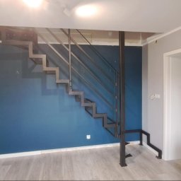 Szymon Klawikowski - Nowoczesne schody metalowe o konstrukcji wspornikowej, z ażurową balustradą, umieszczone w minimalistycznym wnętrzu z akcentem granatowej ściany.