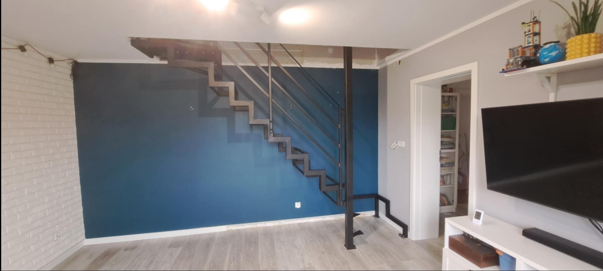 Nowoczesne schody metalowe o konstrukcji wspornikowej, z ażurową balustradą, umieszczone w minimalistycznym wnętrzu z akcentem granatowej ściany.