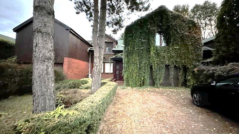 Dom jednorodzinny z zielonym dachem i fasadą porośniętą bluszczem, widoczny z perspektywy podjazdu. Obok zaparkowany czarny samochód.