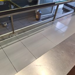 UT-R Marek Przyybylski - Półka w chłodni z metalową miską i butelką oleju w tle, widok z góry. Czysta, wyłożona płytkami podłoga. Minimalistyczny wystrój.