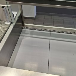 UT-R Marek Przyybylski - Pusta, chłodnicza witryna sklepowa z szarym blatem, widoczna z góry, ukazująca czystość i gotowość do ekspozycji produktów. Metalowe wykończenia i szklana szyba.