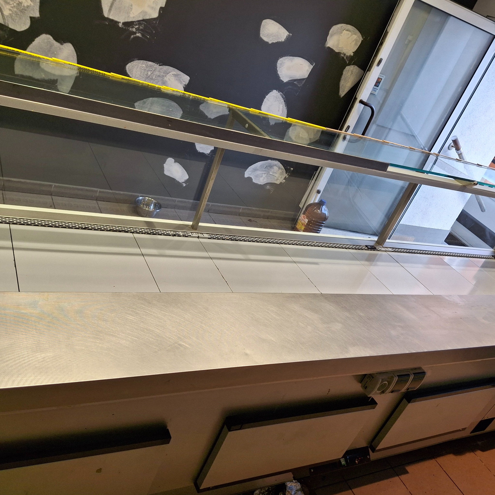 Półka chłodnicza po czyszczeniu, widoczne ślady po umyciu na suficie, metalowa misa i butelka w środku. Perspektywa z dołu, oświetlenie mieszane.