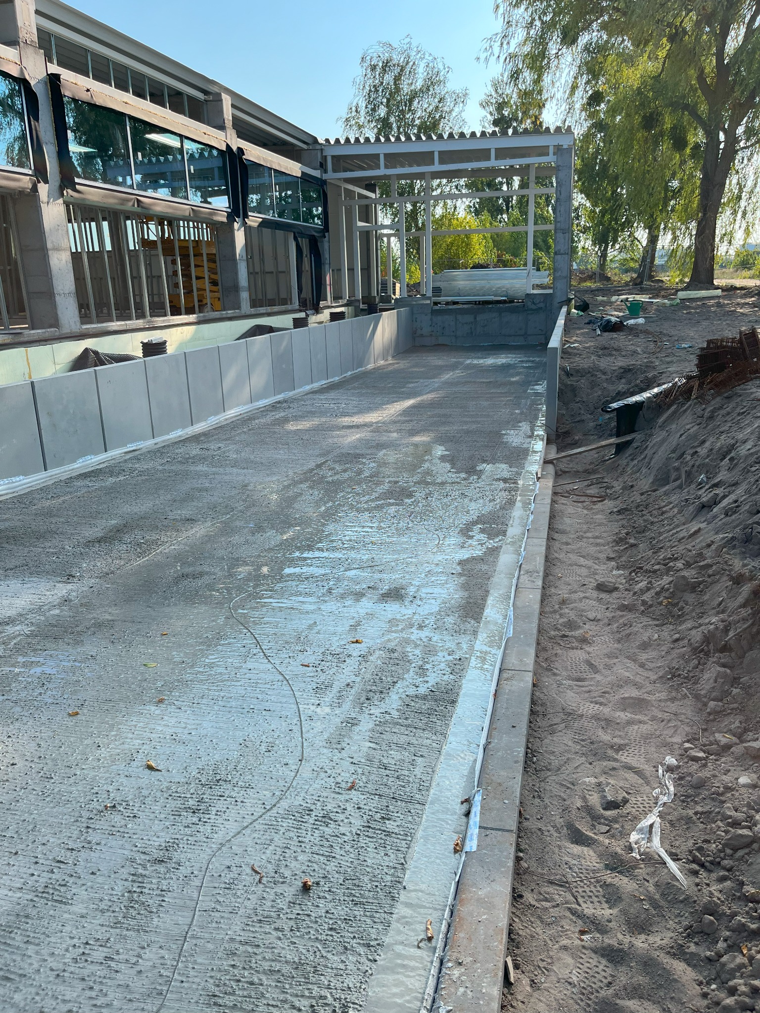 Wylana, mokra posadzka betonowa wewnątrz konstrukcji budynku w stanie surowym otwartym, z widocznym zbrojeniem i elementami szalunku. Prace budowlane w toku.