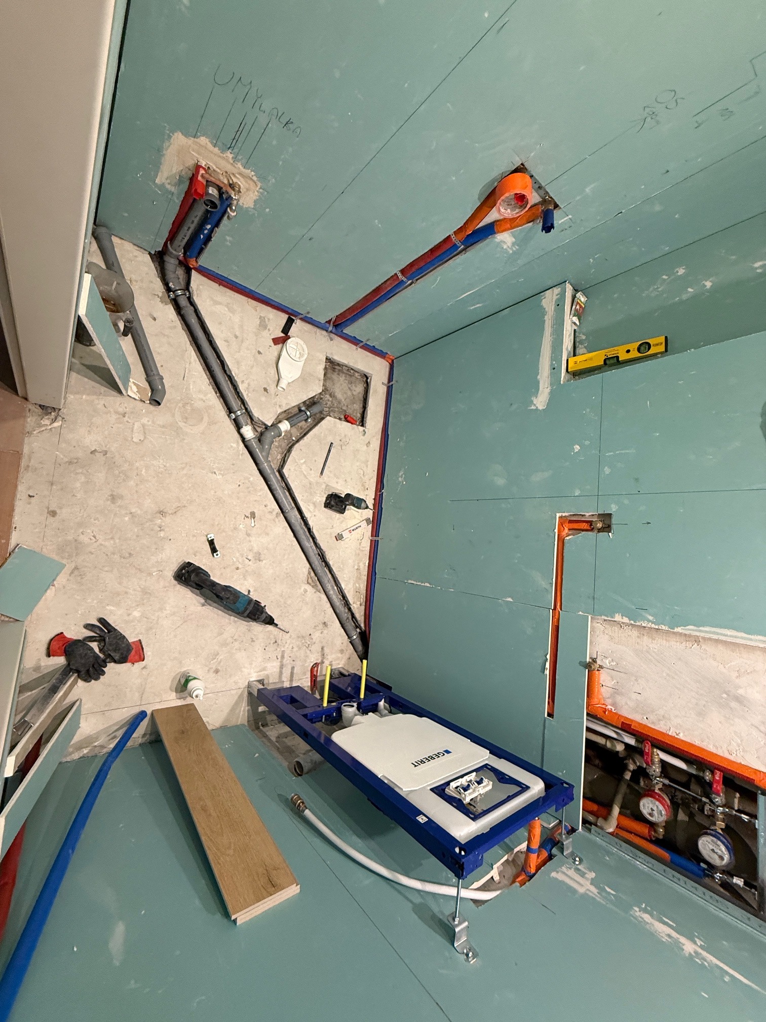 Instalacja sanitarna w trakcie montażu: rury, stelaż podtynkowy WC Geberit, narzędzia. Ściany pokryte płytami gipsowo-kartonowymi. Widoczne podejścia wodne i kanalizacyjne.