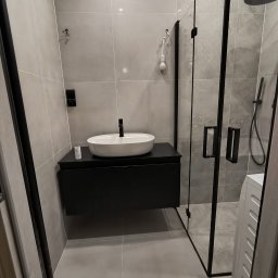 Krzysztof Stachnio - Nowoczesna łazienka w szarościach z czarnymi akcentami: owalna umywalka na szafce, kabina prysznicowa walk-in z czarnymi profilami i płytki w odcieniach szarości.