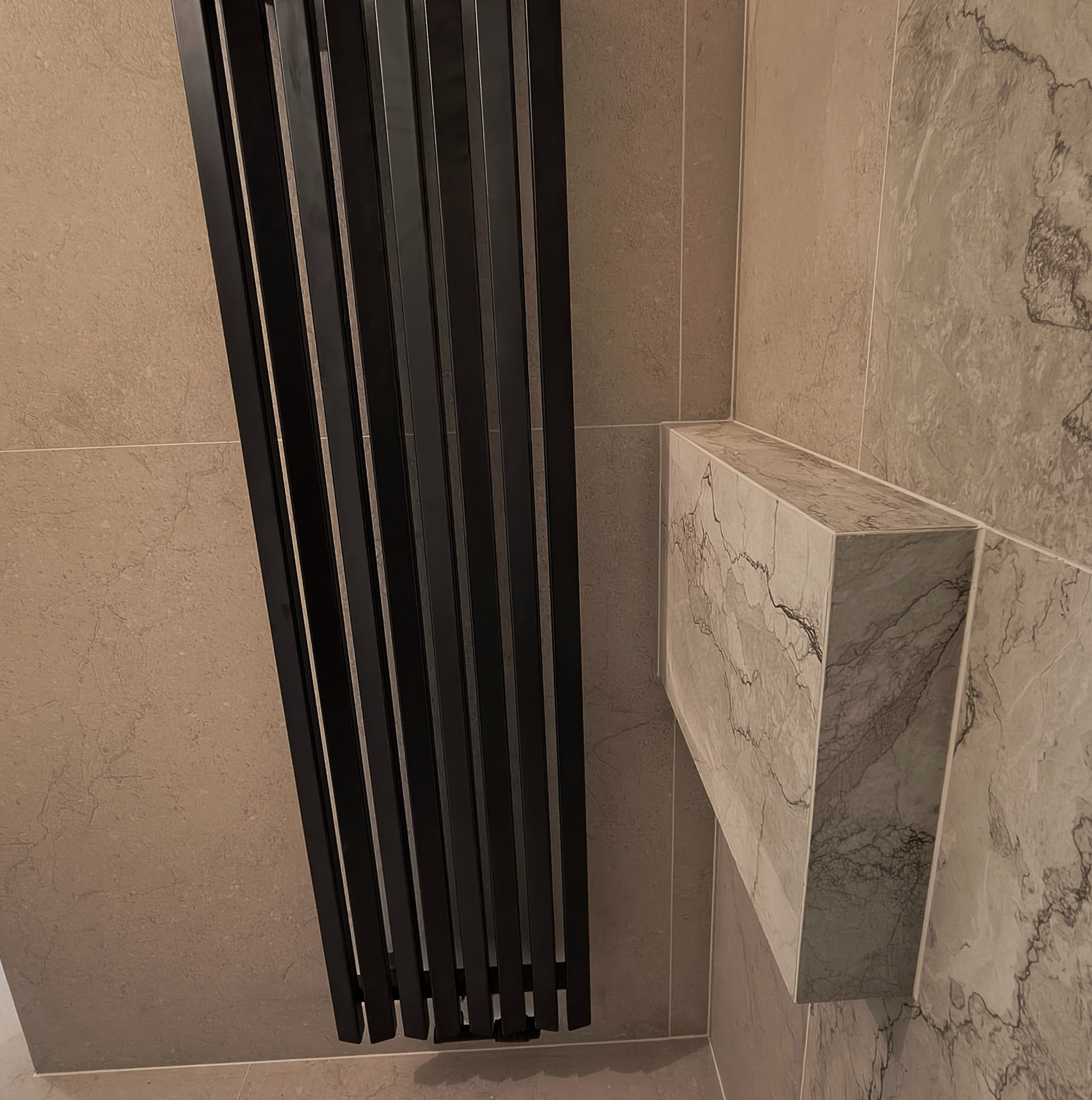 Nowoczesna łazienka z grzejnikiem drabinkowym i obudową umywalki z płytek imitujących marmur. Szare płytki ścienne tworzą spójną całość.