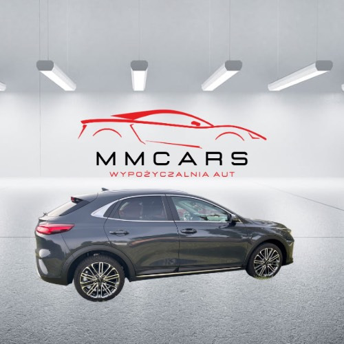 Szary crossover Kia XCeed na tle ściany z logo MM Cars Wypożyczalnia Aut, w jasnym garażu z oświetleniem LED. Widok z boku, felgi aluminiowe.
