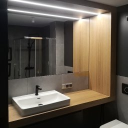 MONT - MEBEL MICHAŁ PAWŁOWSKI - Nowoczesna łazienka z drewnianą szafką i blatem, białą umywalką oraz podświetlanym lustrem. W tle widoczna kabina prysznicowa.