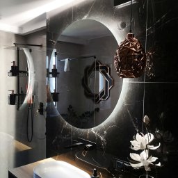 MONT - MEBEL MICHAŁ PAWŁOWSKI - Elegancka łazienka w Raszynie z okrągłym lustrem LED, czarnymi płytkami marmurowymi i drewnianą szafką pod umywalkę. Nowoczesny design z kwiatami i lampą.