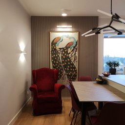 MONT - MEBEL MICHAŁ PAWŁOWSKI - Elegancka jadalnia z czerwonym fotelem uszakiem i stołem z blatem imitującym marmur. Na ścianie dekoracyjny panel z obrazem pawi, nowoczesna lampa sufitowa.