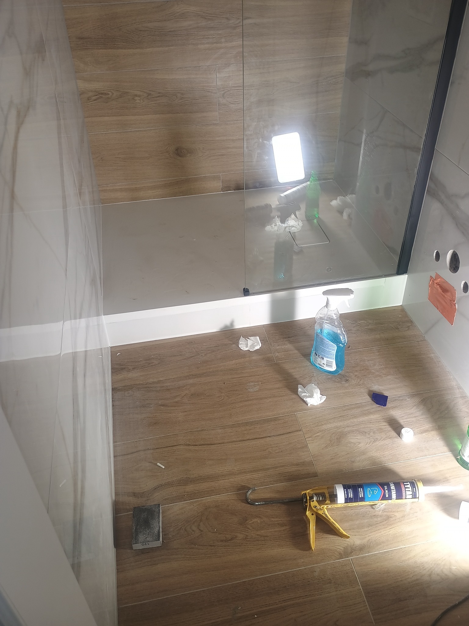 Wykończona kabina prysznicowa z drewnopodobnymi płytkami, widoczne narzędzia i środki czystości, podkreślające etap końcowy prac glazurniczych.