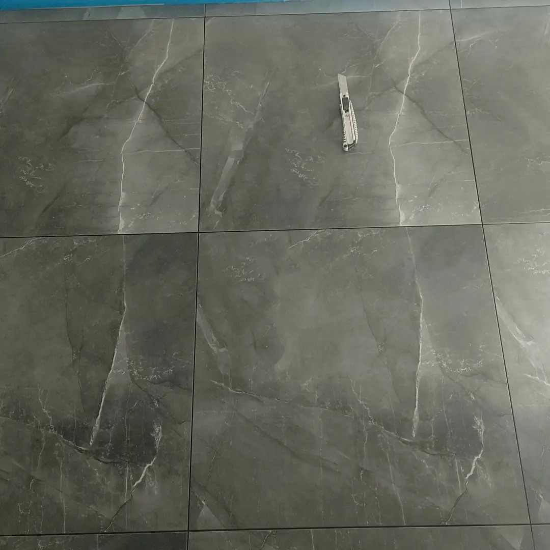 Ułożone, szare płytki podłogowe imitujące marmur, z widocznym nożykiem do cięcia płytek. Minimalistyczny design, regularny wzór, precyzyjne fugi.