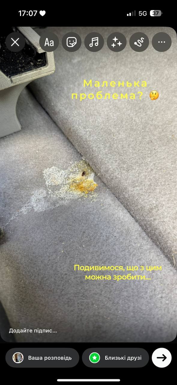 Szara tapicerka samochodowa z widocznym, brązowo-żółtym zabrudzeniem. Tekst w języku ukraińskim sugeruje problem i chęć jego rozwiązania.