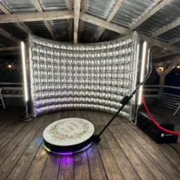 Srebrna, dmuchana fotobudka z oświetleniem LED i obrotową platformą na drewnianej podłodze pod zadaszeniem, gotowa do użycia na imprezie.