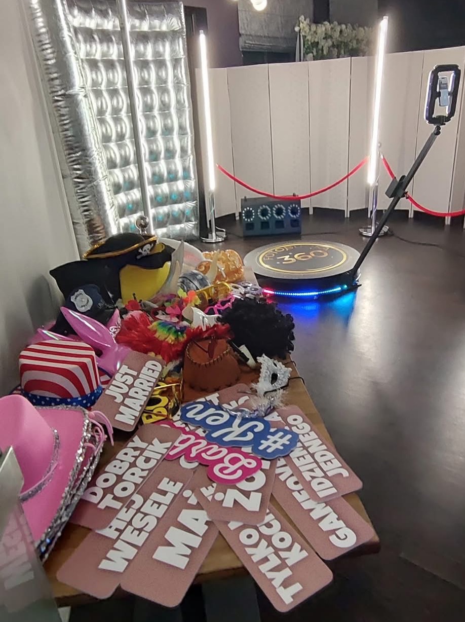 Atrakcje na imprezę: fotobudka 360 z rekwizytami (kapelusze, peruki, napisy) i dekoracjami (ścianka, oświetlenie LED). Gotowość do zabawy, perspektywa z góry.