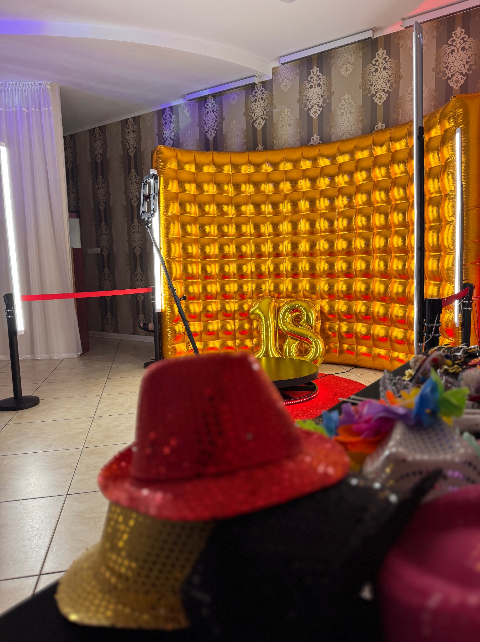 Zestaw fotobudki z złotym tłem, balonem '18' i rekwizytami (kapelusze) na pierwszym planie, gotowy do użycia podczas imprezy osiemnastkowej.