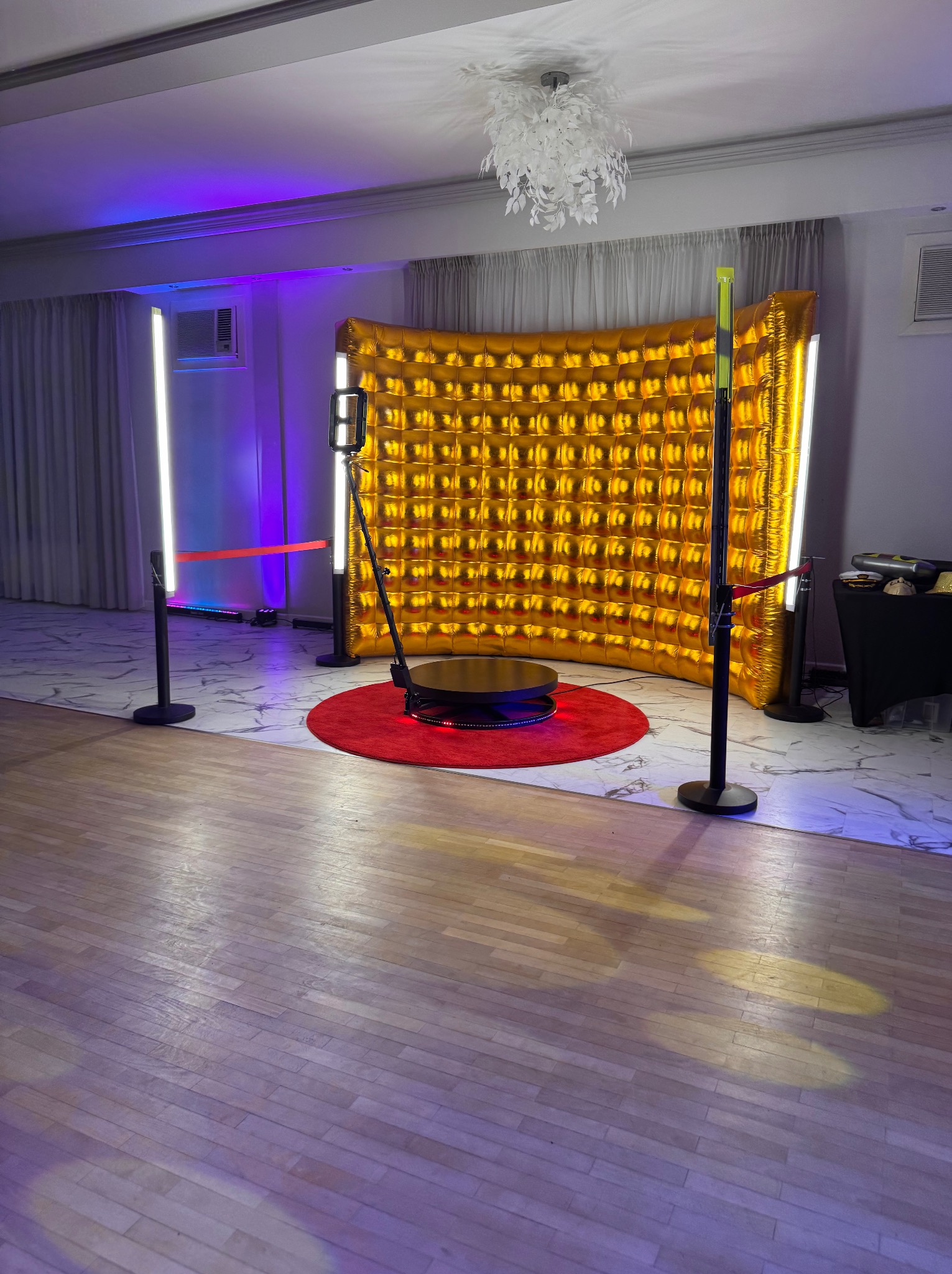 Złota ścianka dmuchana z podświetleniem LED i obrotową platformą na czerwonym dywanie, tworząca tło do nagrywania wideo na imprezach.