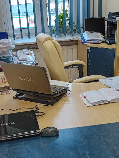 Biuro z beżowym krzesłem, laptopem Sony Vaio na podstawce i otwartym notatnikiem. Na biurku leży laptop Toshiba i myszka. W tle okno z żaluzjami.