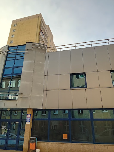 Nowoczesny budynek biurowy z elementami szkła i aluminium, widoczny z dołu, z fragmentem starszego budynku w tle i pomarańczowym akcentem na elewacji.